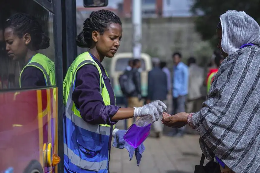 A volunteer provides hand sanitizer to passengers entering a bus as a precaution against the spread of the new coronavirus in the capital Addis Ababa, Ethiopia © AP Photo/Mulugeta Ayene